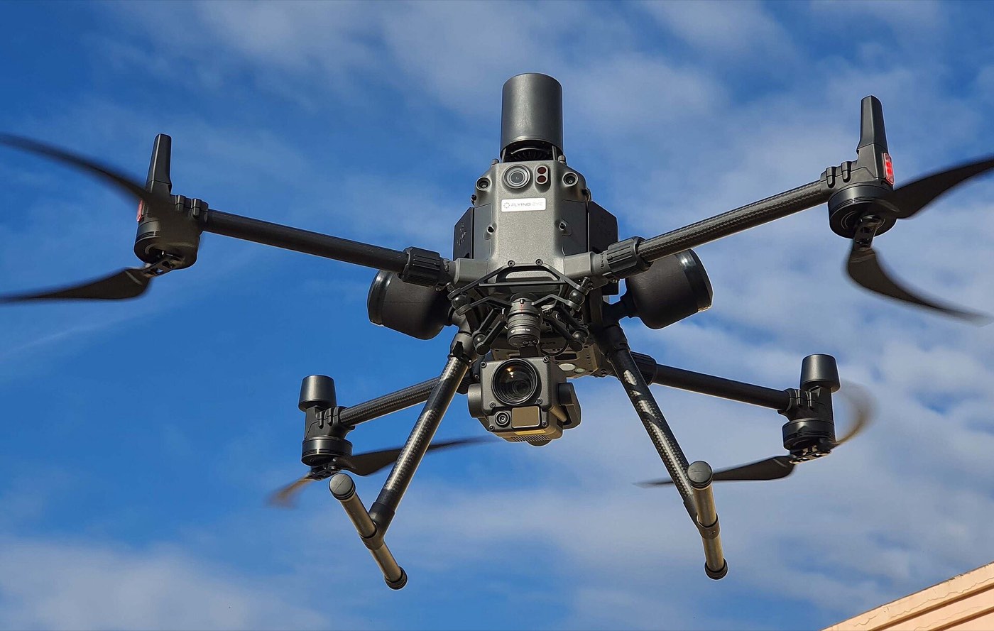 Drone professionnel à quatre rotors en vol, vu de dessous, ciel bleu